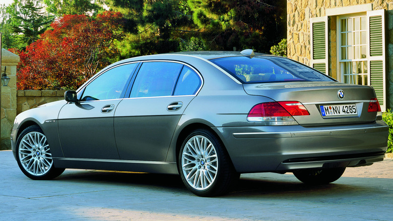 A green 2006 BMW 7 Series parked in front of a building, a wall and trees