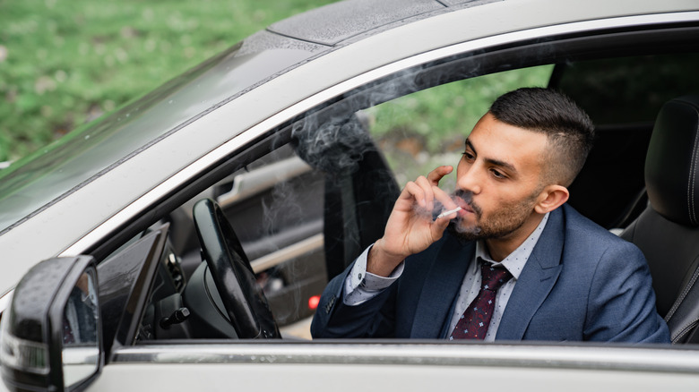 Man in a business suit smoking a cigarette while sitting in the driver's seat