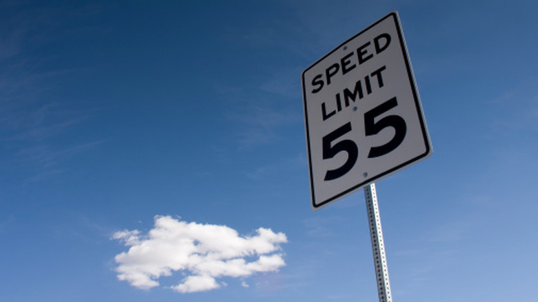 A 55-mph speed limit sign contrasted against a blue sky on a highway