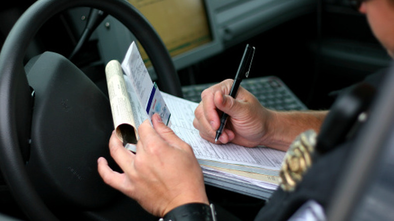 A police officer writes a citation for a motorist while handling the offending driver's license