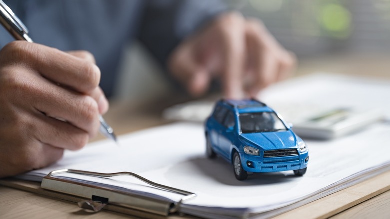 A person holding a pen near a clipboard and toy car.
