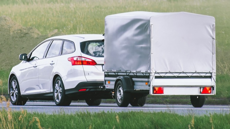suv towing covered trailer on a road