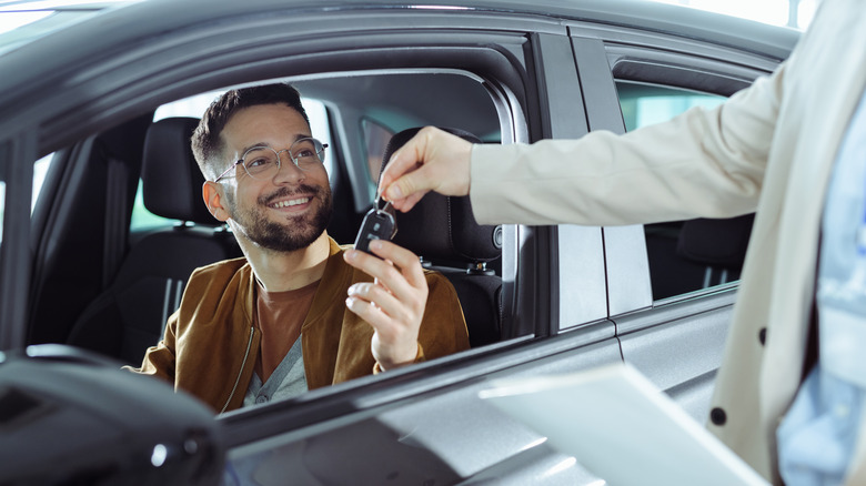 A man receives the keys to a new car from the salesperson at a dealership