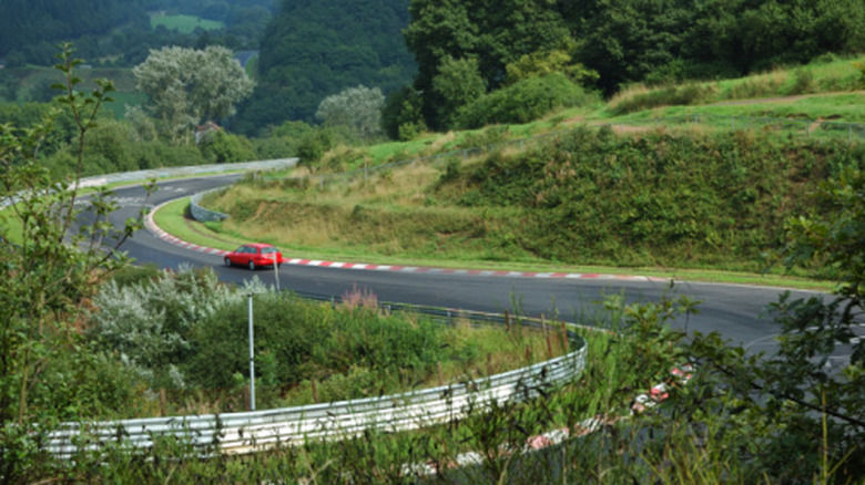 A lonely hatchabck car takes on a sweeping s curve at the Nurburgring.