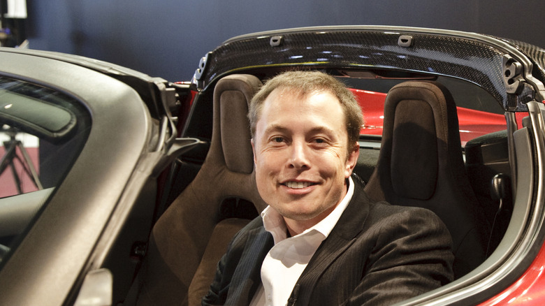 Elon Musk sitting in an original Tesla Roadster