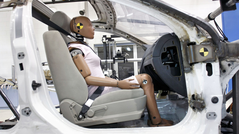 Crash test dummy sits strapped into the front passenger seat of a vehicle undergoing safety testing.