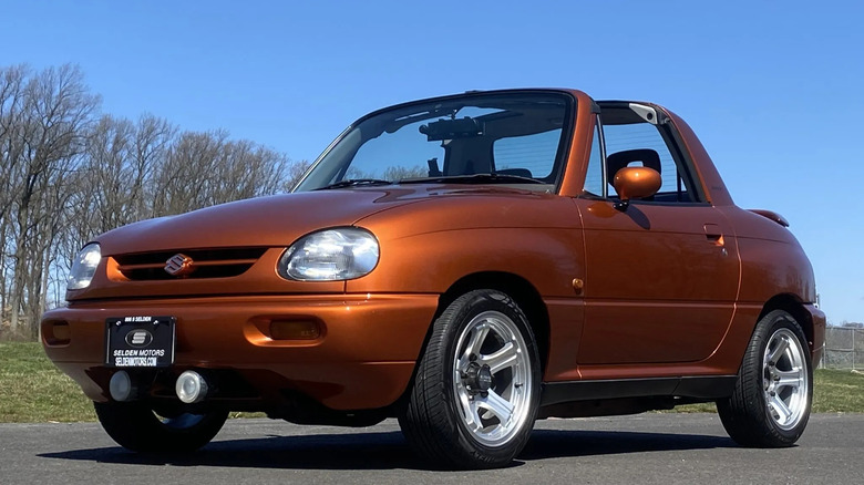 Front three quarters shot of a copper colored Suzuki X-90 parked on asphalt in front of a blue sky and trees with no leaves