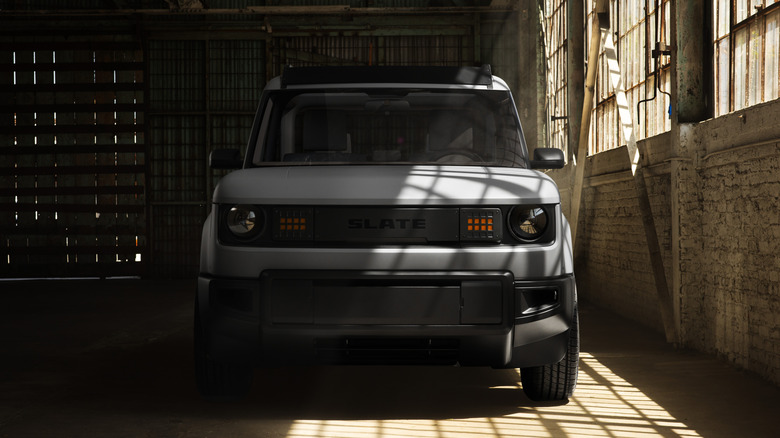 The front end of a Slate truck in an empty brick warehouse with large lead glass windows pouring light onto the driver's side of the vehicle.