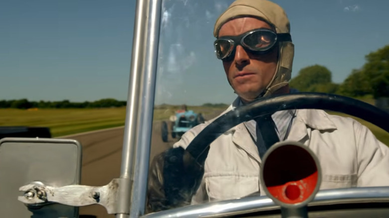 The properly outfitted racing driver Henry Talbot behind the wheel of his racing car, just from the driver's window on track, in an episode of Downton Abbey.