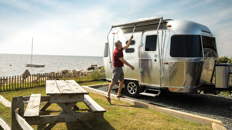 Man setting up awning of 2020 Airstream Caravel trailer near lake