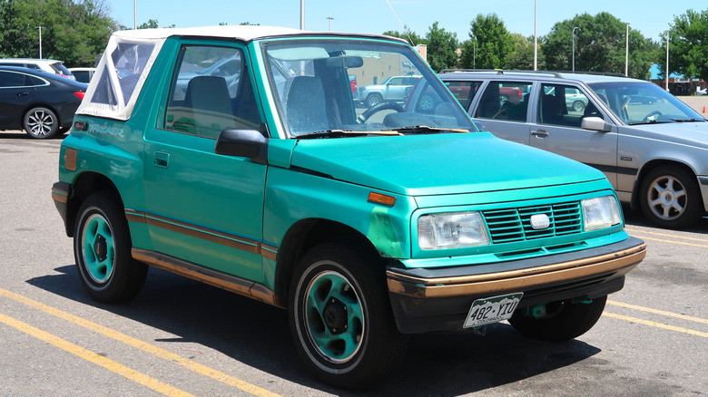 A turquoise Geo Tracker parked in the sun in a shopping center parking lot