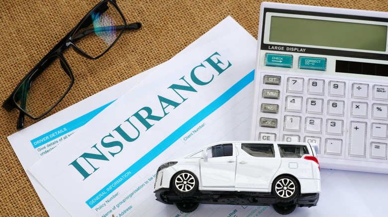 Close-up shot of an insurance document, toy car, and calculator placed neatly on a textured surface