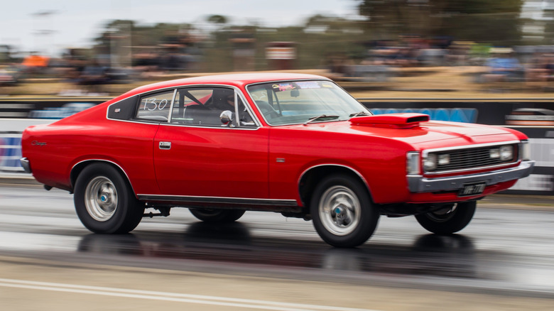 Red classic car accelerates on drag strip.