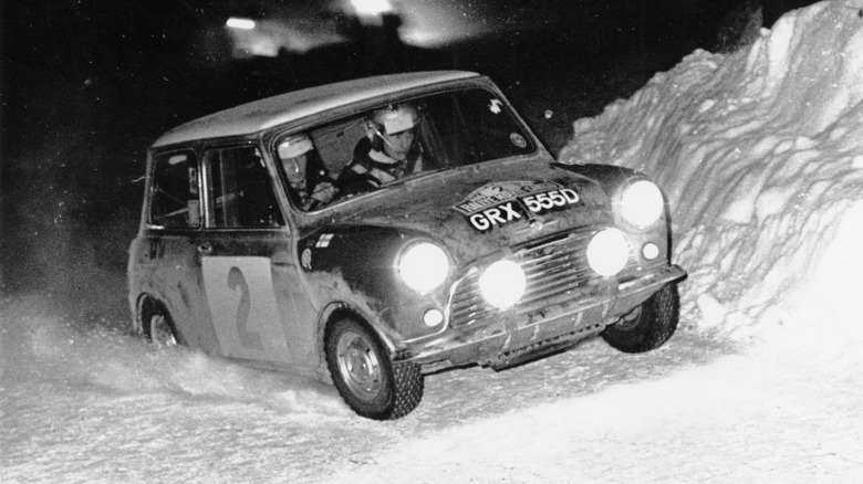 A black and white image of a Mini Cooper S driving in heavy snow at the 1966 Monte Carlo Rally.