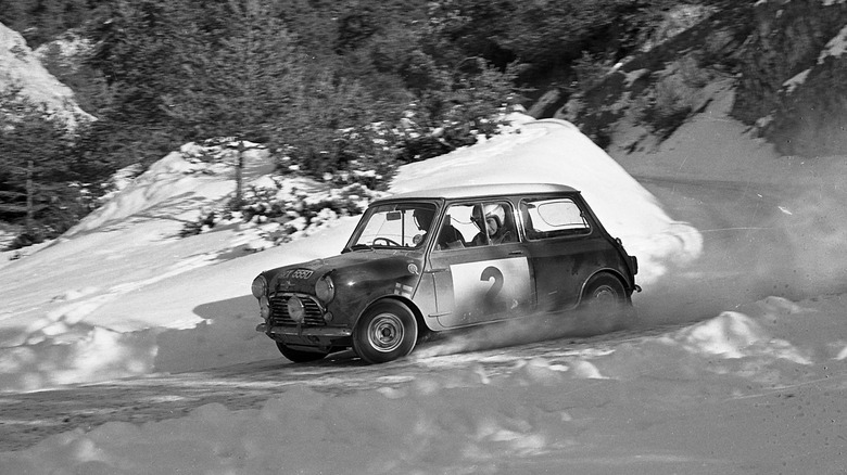 A black and white image of a Mini Cooper S taking a tight curve in the snow at the 1966 Monte Carlo Rally.