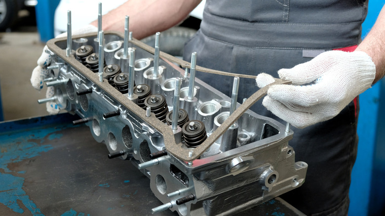एक मैकेनिक कार में सिलेंडर हेड असेंबली स्थापित करने से पहले उसकी जाँच करता है।