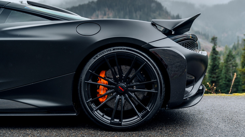 A rear-end side view of a black McLaren 720S supercar in the rain with mountains in the background