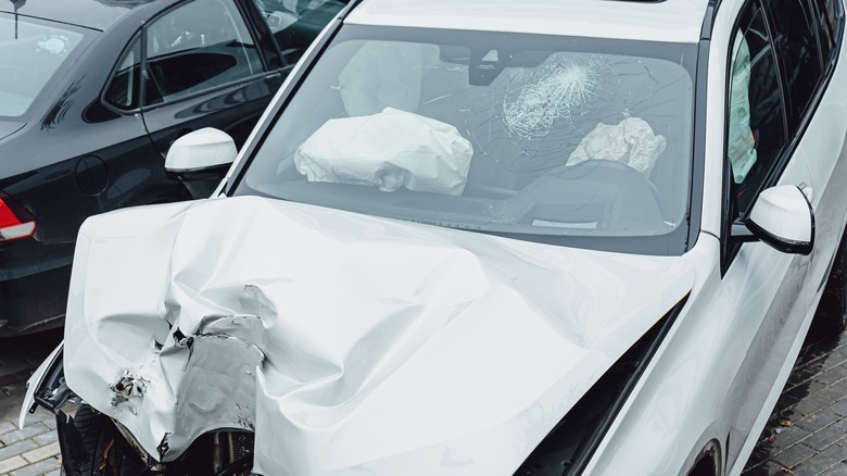 A white car after a frontal impact showing both airbags deployed but the windshield still intact and in place,