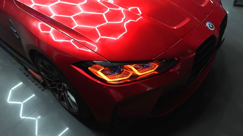 A red BMW M4 with red headlights in a garage with hexagon lighting