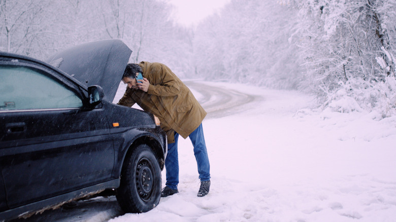 A man struggling to start his car in winter
