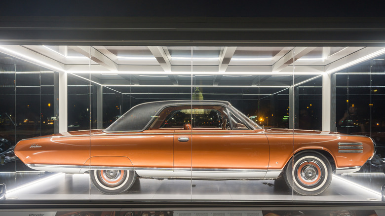 An orange Chrysler Turbine Car sits behind glass in an outdoor display at night