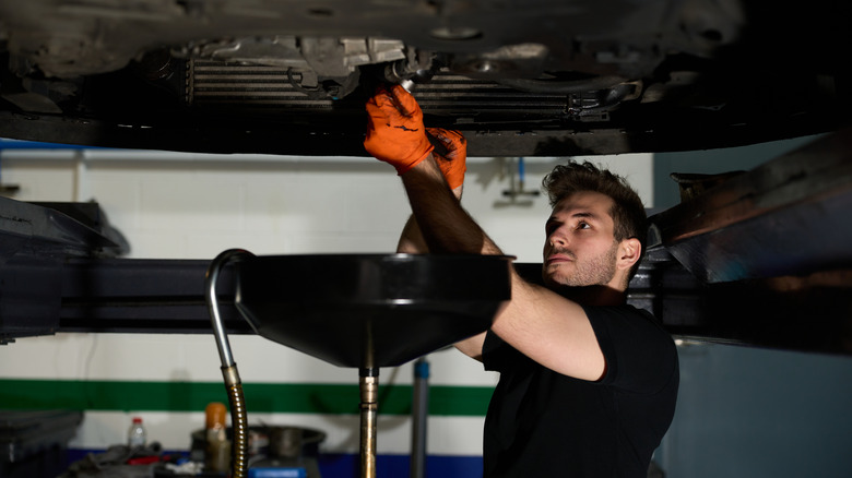 Mechanic loosening the oil drain plug to drain the old engine oil