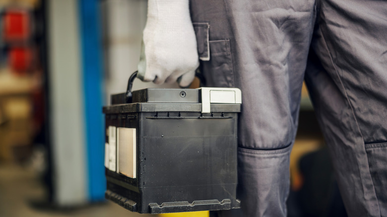 A gloved technician carrying a lead-acid car battery.