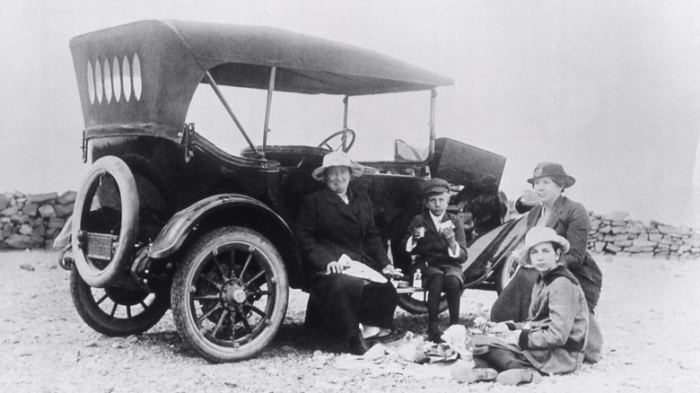 Tourists eating beside a car along a roadside.