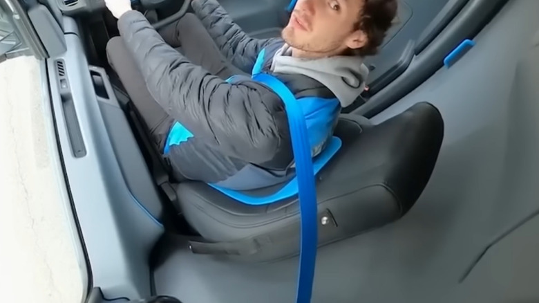 An Amazon delivery driver wearing a bright blue seat belt in a Rivian electric delivery vehicle.