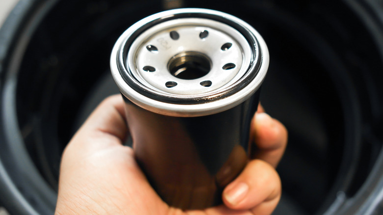A technician holding a black engine oil filter above an oil drain pan.