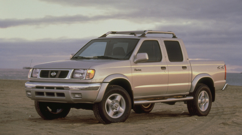 A front 3/4 shot of a gold 2000 Nissan Frontier with roof rack parked on sand