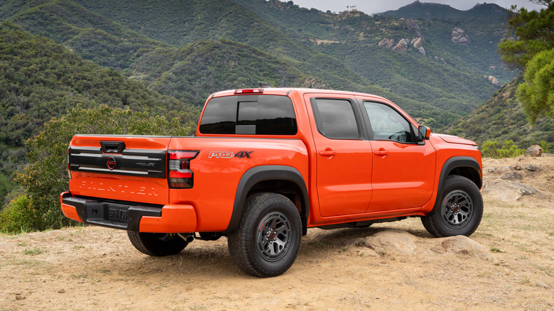 A rear 3/4 shot of an orange 2026 Nissan Frontier PRO-4X parked on sand in front of hills