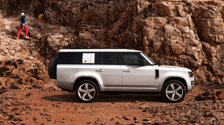 Land Rover Defender 130 parked in front of rocks with rock climber in background
