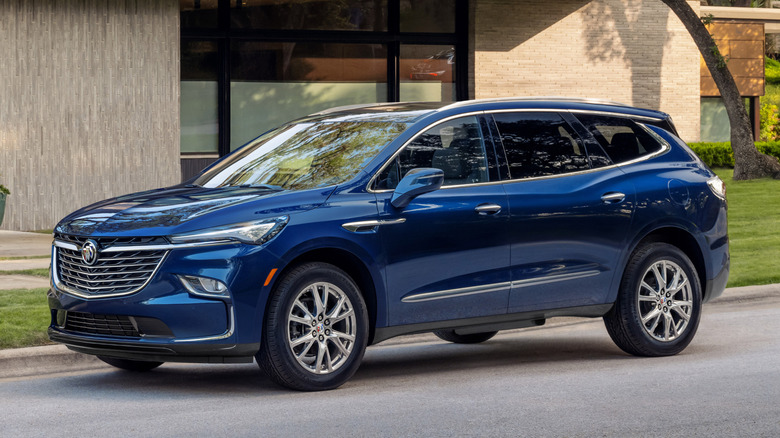 Driver front 3/4 view of 2023 Buick Enclave in Emperor Blue Metallic parked curbside with house in background