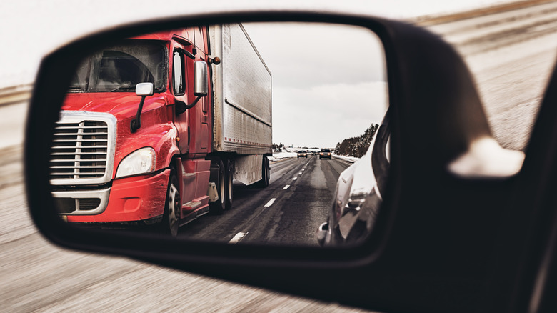 A car's side mirror showing a semi truck in the other lane of a highway