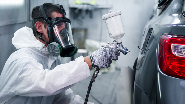 A person painting a car while wearing a mask