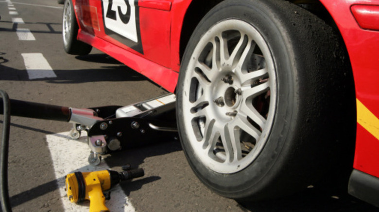 Red race car getting front right wheel changed in pits