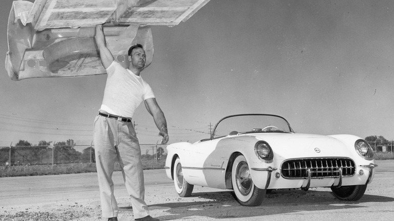 A man holds up the 1953 Corvette's fiberglass body structure in front of a white 1953 Corvette