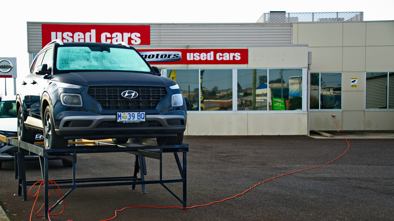 A Hyundai sitting on a portable lift in front of a used car dealership in Australia.