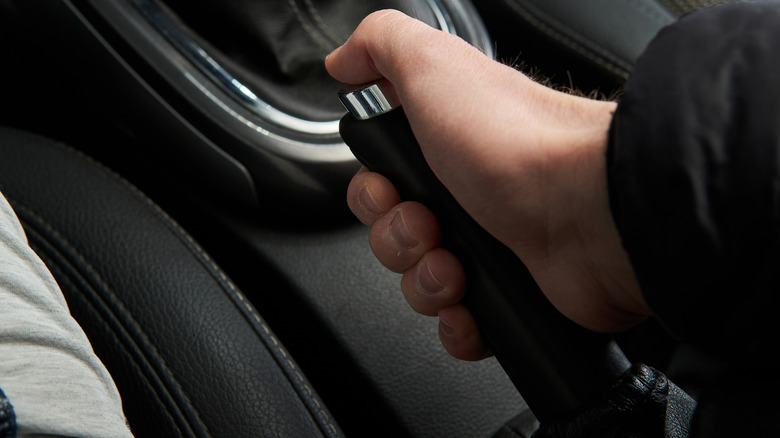 A man is holding and pulling up nan parking brake grip successful a car pinch a achromatic interior.