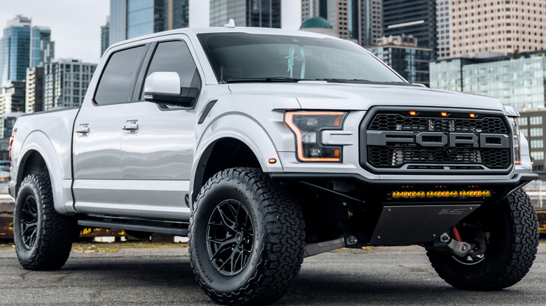 A white 2018 Ford F-150 Raptor parked with skyscrapers in the background.