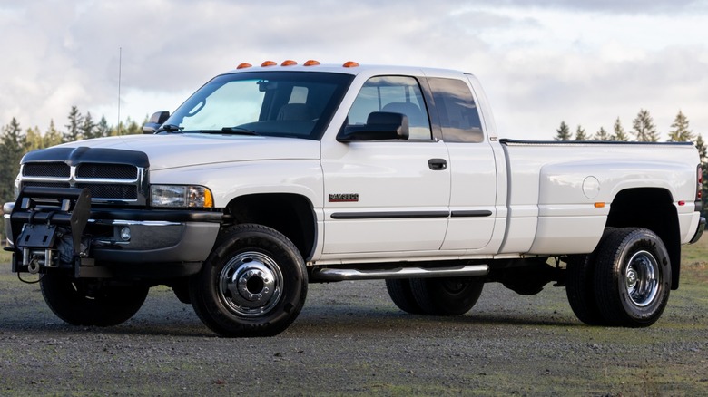 A white diesel pickup truck on gravel in front of scrubby pines