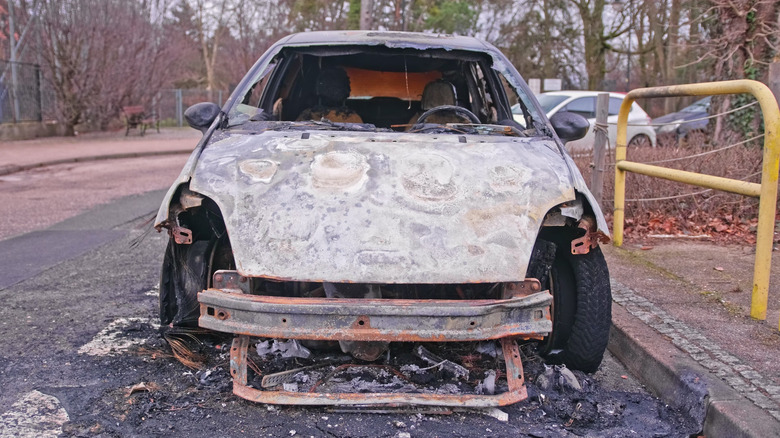 A burnt and broken electric vehicle parked next to a curb