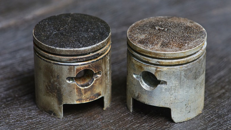 A pair of used pistons on a wooden table.