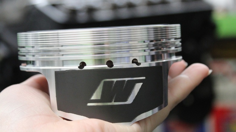 Someone holding a lightweight forged piston in the palm of their hand.