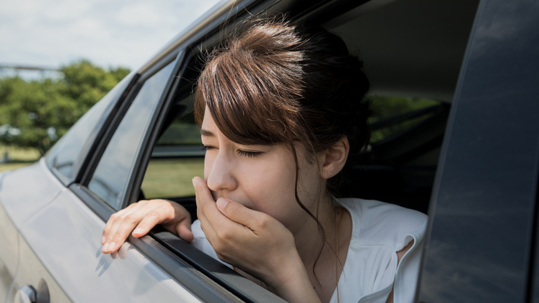 Woman getting carsick and leaning her head out of a window with a hand over her mouth