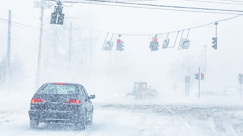 Car stopped a red light in snow with the traffic lights blowing in the wind.