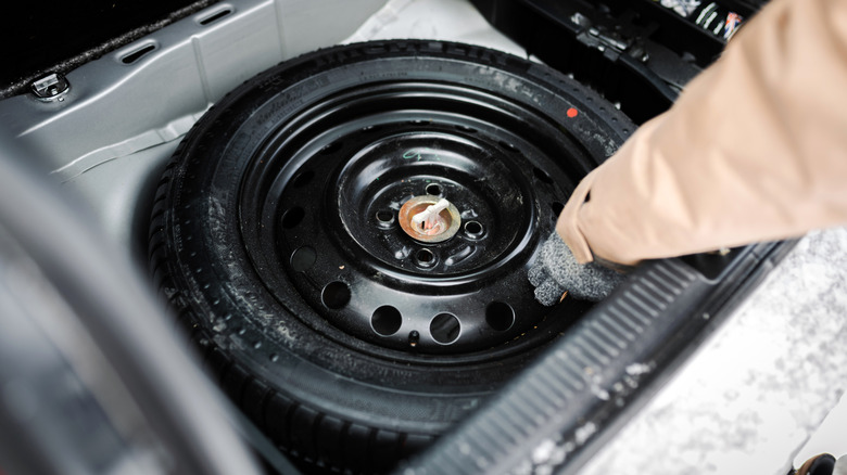 A driver reaches for their spare tire in their car's trunk.