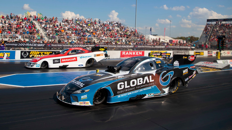 two dragsters racing in front of a large crowd