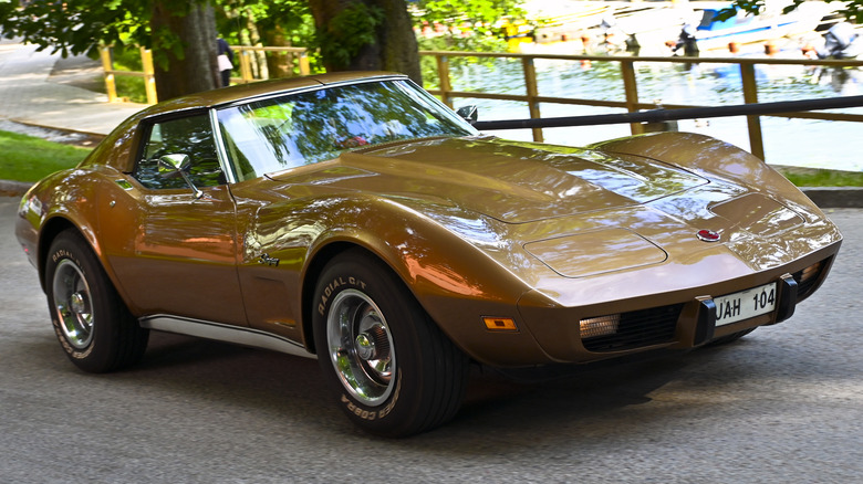 A 1975 Corvette Stingray in bronze, in front of trees and water